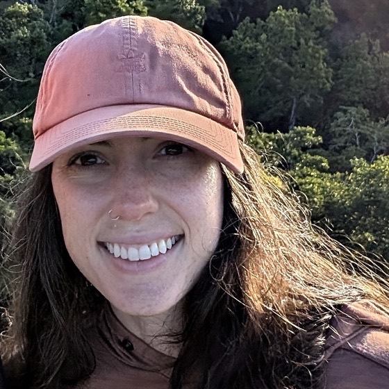 Alanis Loftin, smiling in a ball cap on a forested hillside
