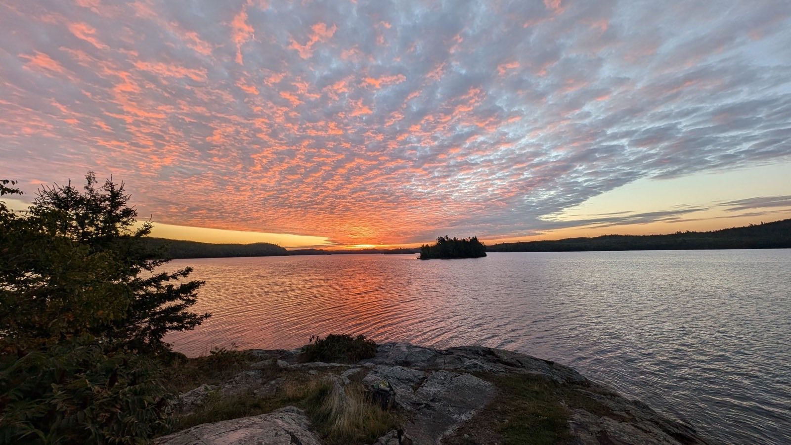 Pink and orange sunset over a lake, seen from a rock outcrop on the shore